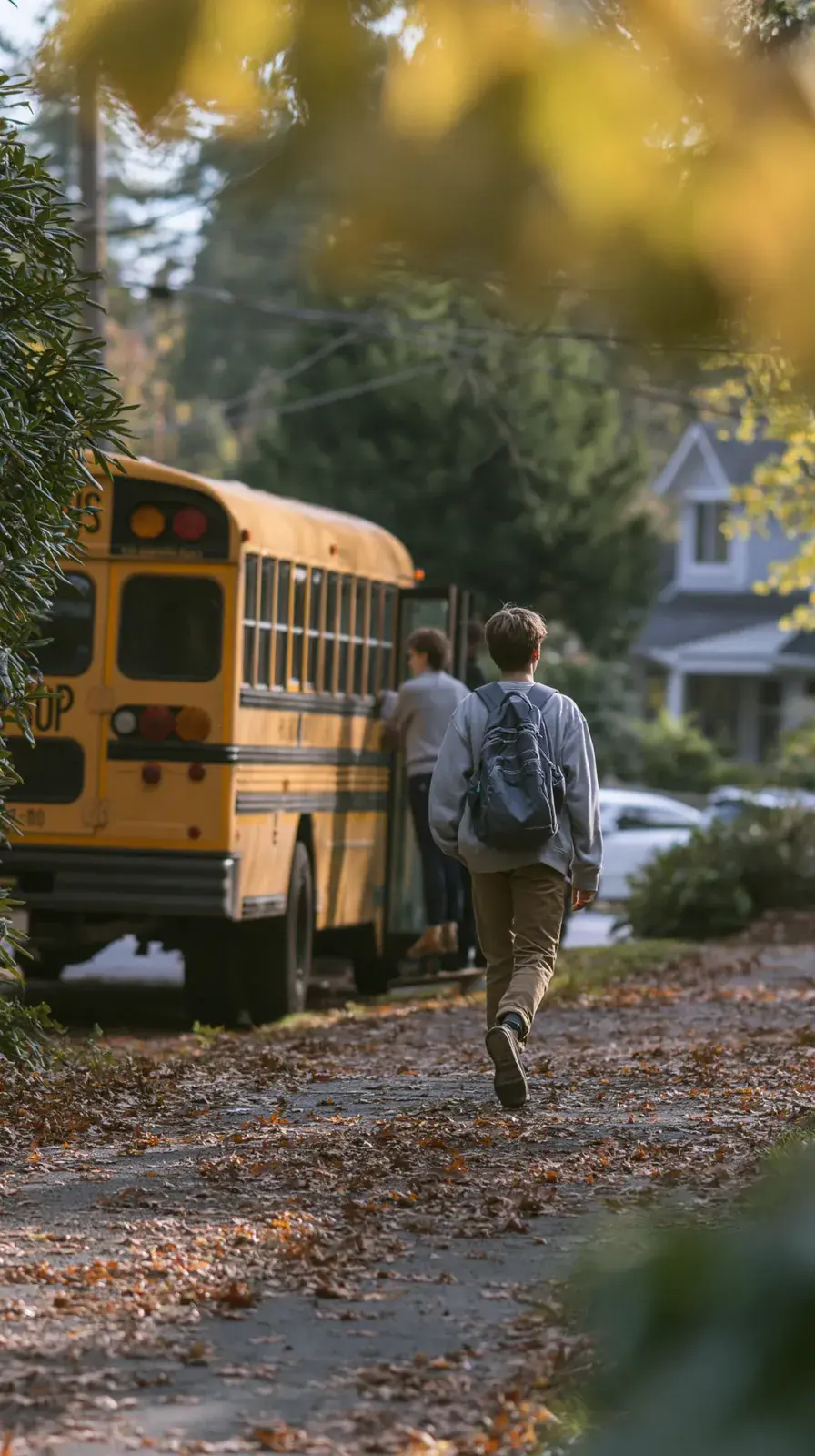 Two students walking a leaf-covered sidewalk toward the waiting bus.