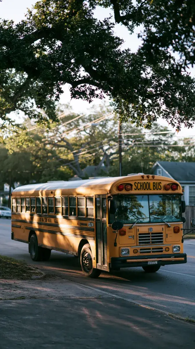 A single bus at the curb of a residential street under live oaks.