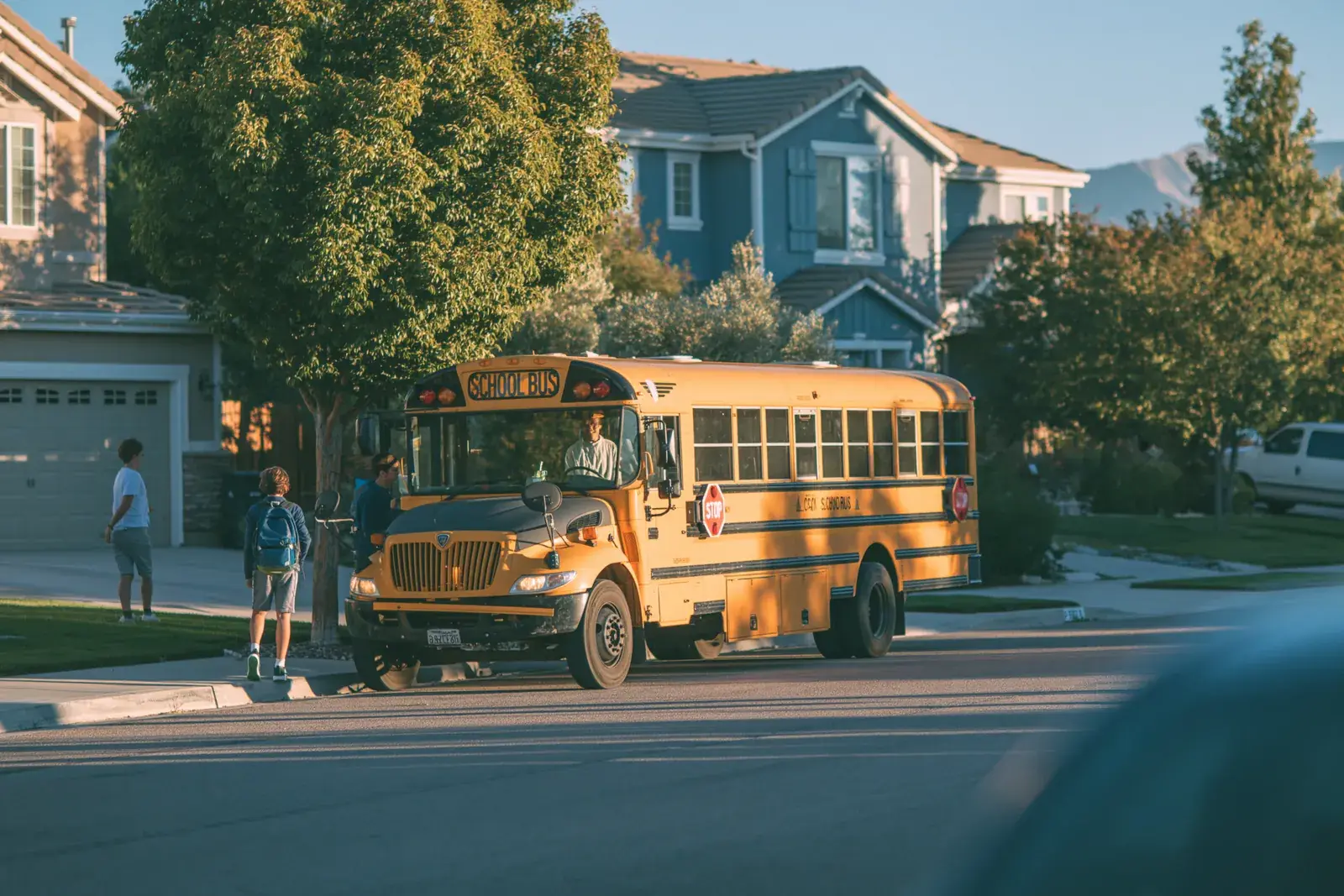A bus stopped on a new subdivision street, riders gathering at the door.
