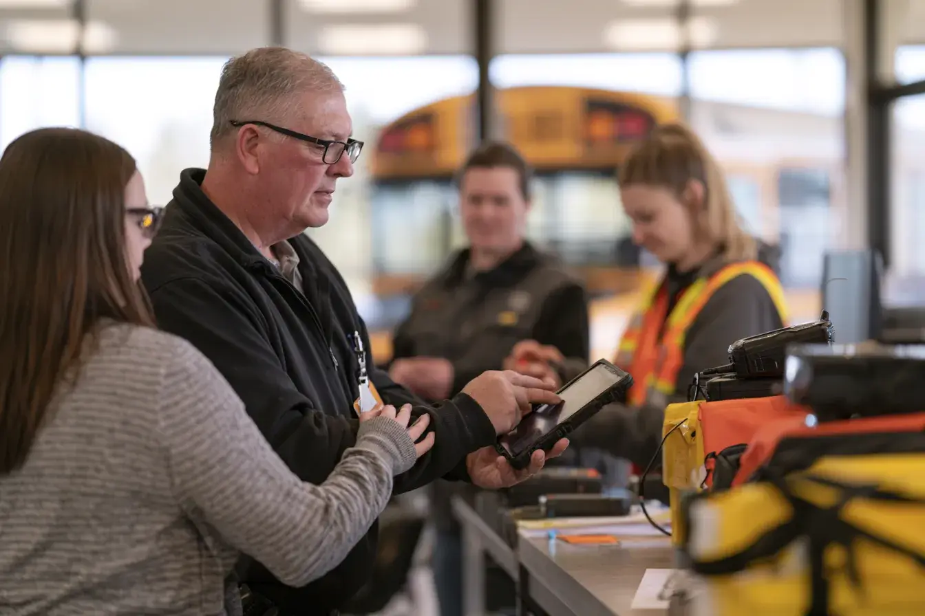 A dispatcher handing a rugged tablet across the counter to a driver.
